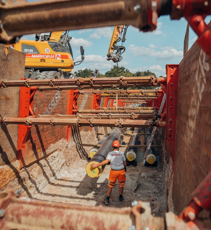 Markgraf-Mitarbeiter bei der Rohrverlegung in einer gesicherten Baugrube mit Bagger im Hintergrund